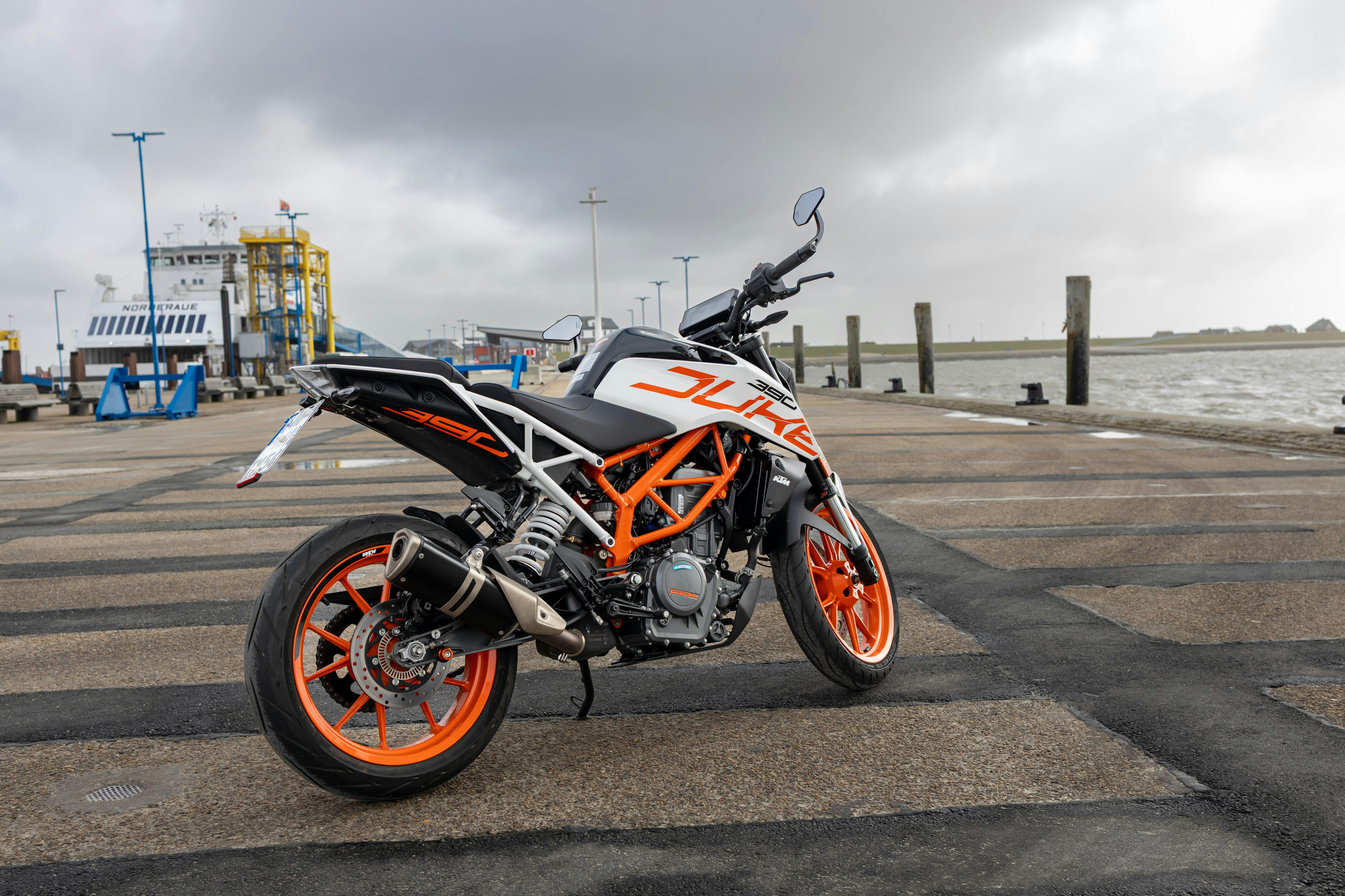 A vibrant KTM Duke motorcycle parked at the picturesque Dagebüll harbor in Germany, showcasing its striking design.