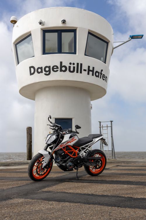 Free A sleek sport motorcycle parked at Dagebüll Hafen's iconic white tower overlooking the coast. Stock Photo