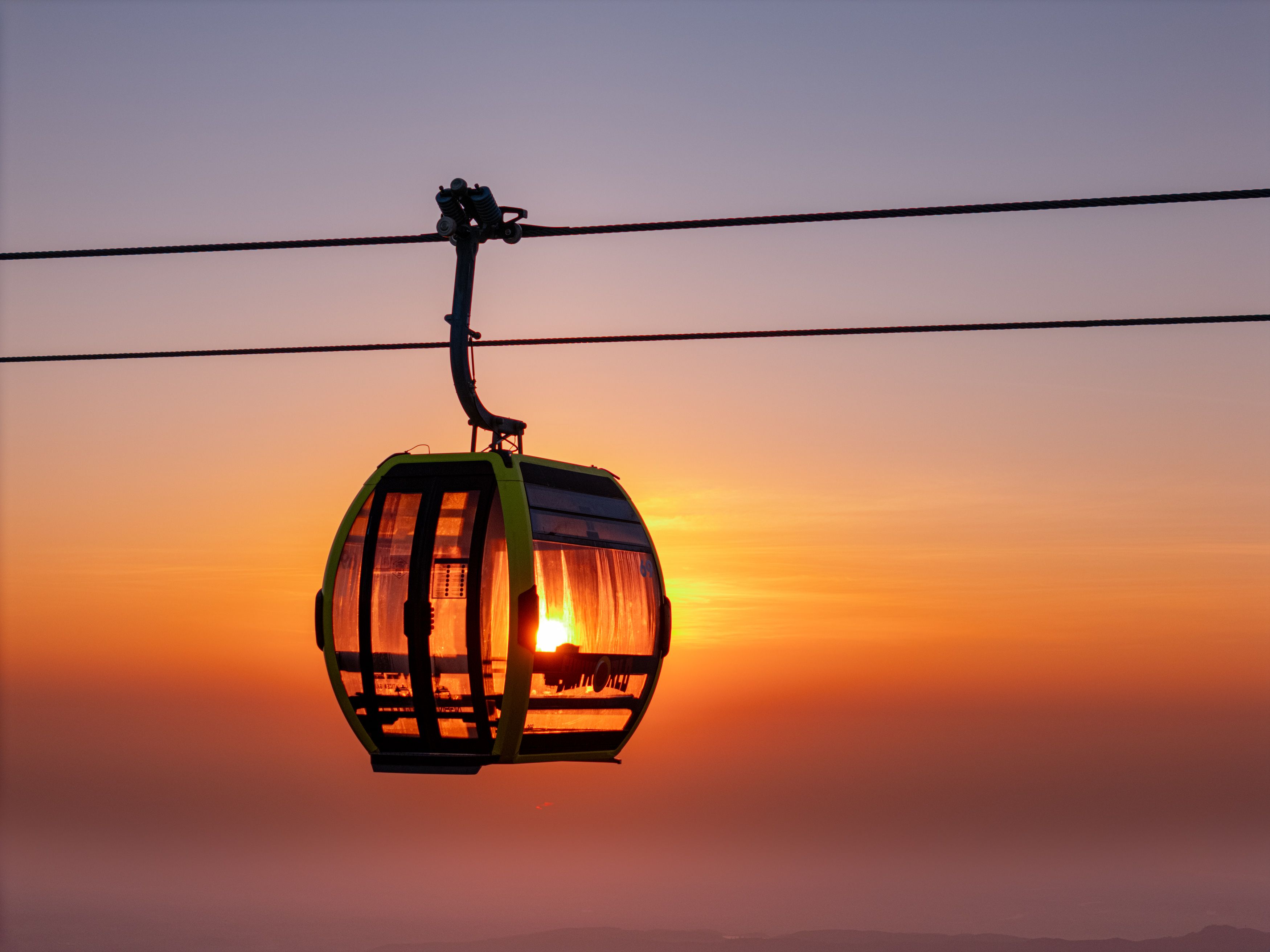 A cable car glides through the sky at sunset, silhouetted against a vibrant horizon.