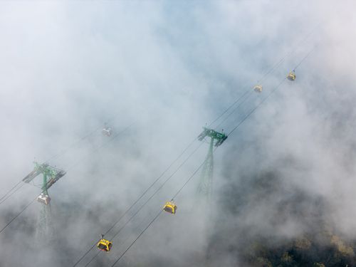 Free Cable cars navigating dense mist over green and rugged mountainous terrain. Stock Photo