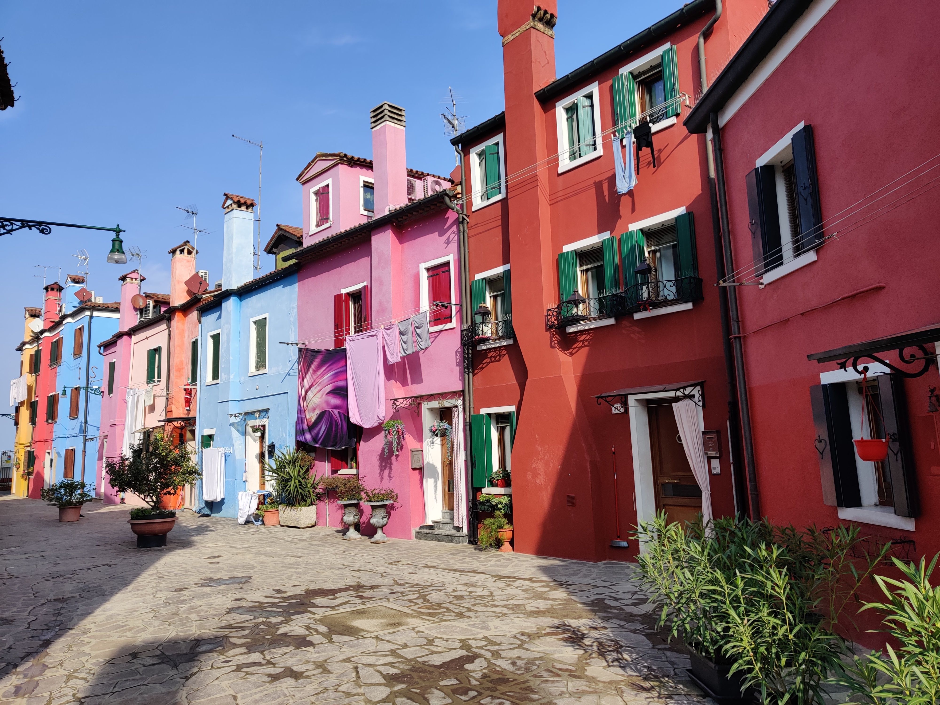 Vibrant houses line a street in Burano, Italy, showcasing colorful facades under a clear blue sky.