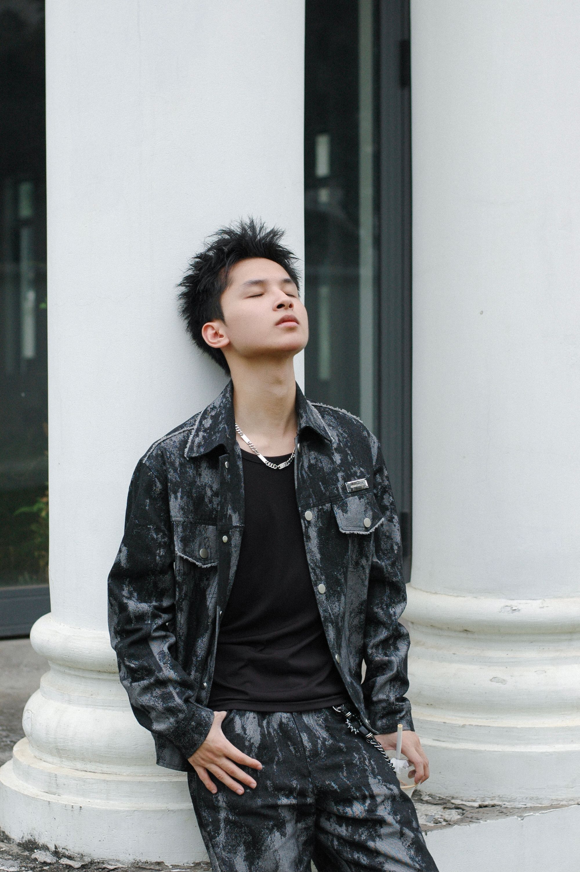 Stylish young man in dark clothing posing thoughtfully against a classic column.