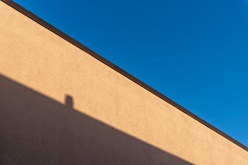 Free A minimalist image of a beige wall casting a shadow against a bright blue sky. Stock Photo