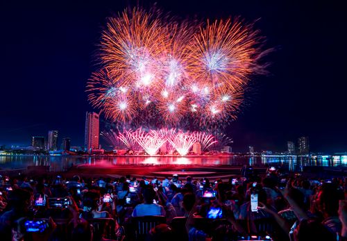 Free Crowd enjoying a colorful fireworks show over a city skyline at night, reflecting on water. Stock Photo