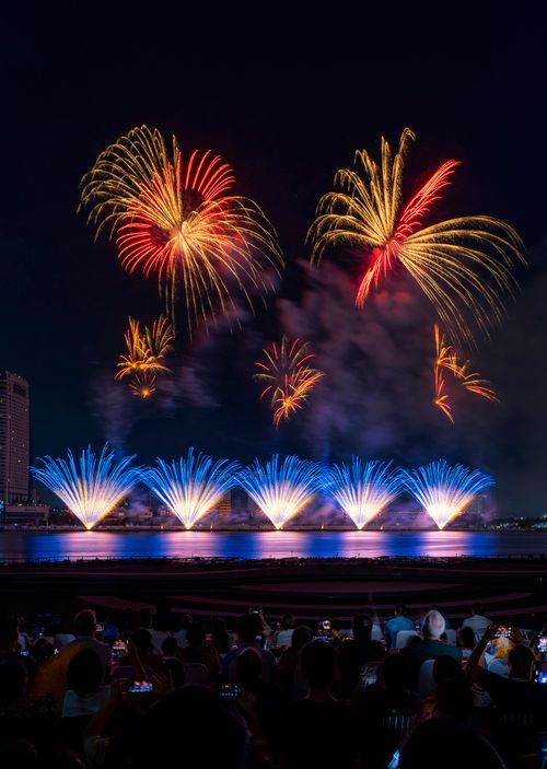 Free Dazzling fireworks light up the night sky over a waterfront with a crowd watching. Stock Photo