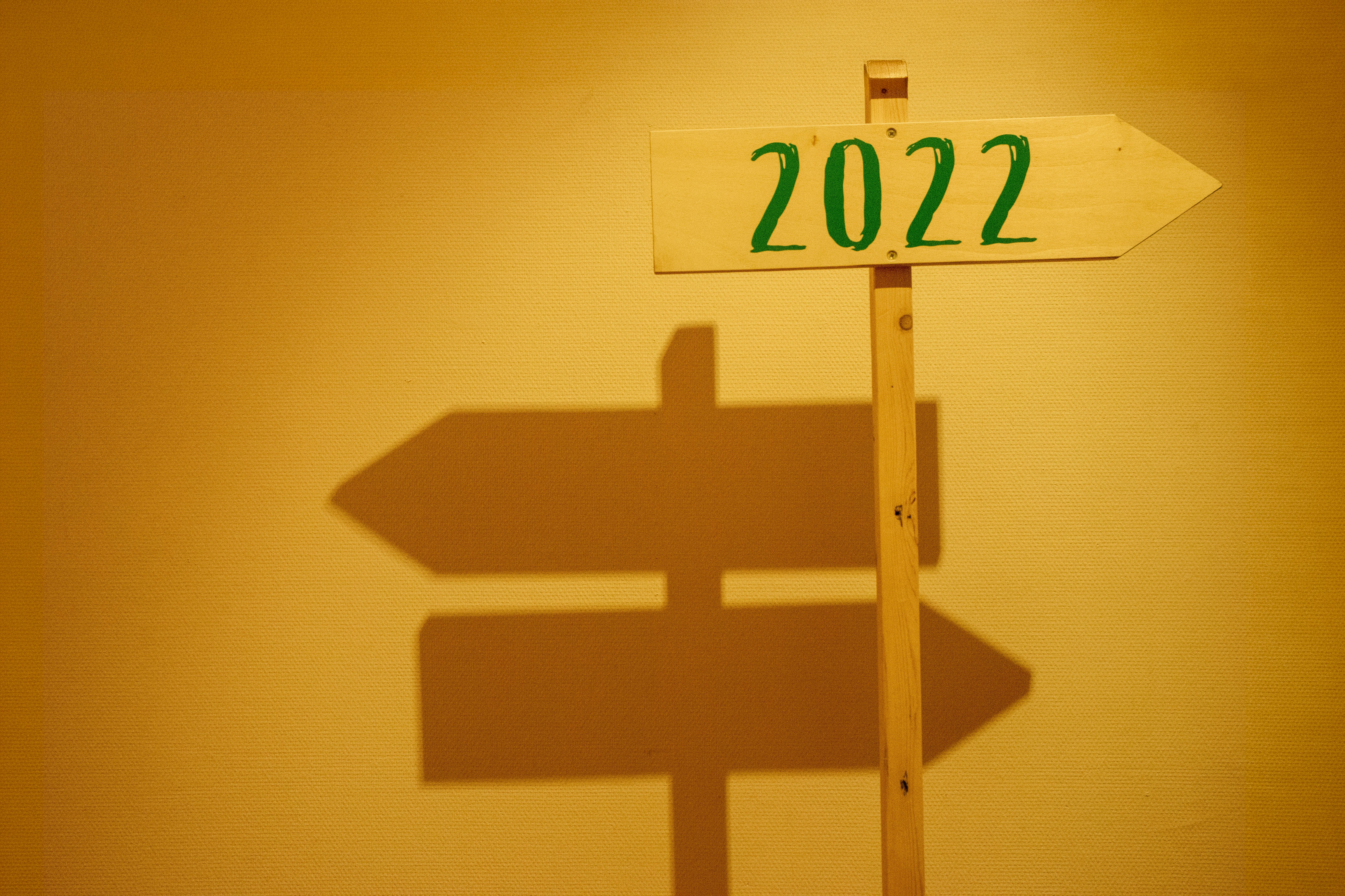 Wooden signpost displaying '2022' with shadow cast on a wall in warm lighting.