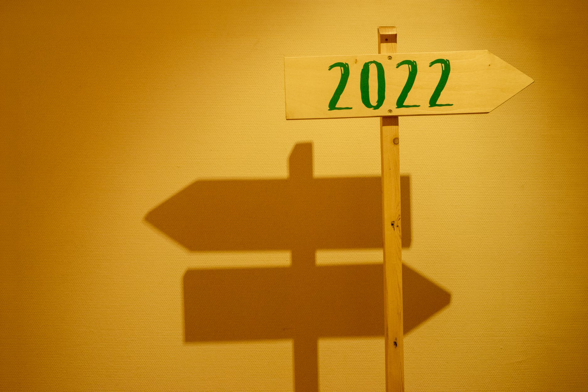 Wooden signpost displaying '2022' with shadow cast on a wall in warm lighting.
