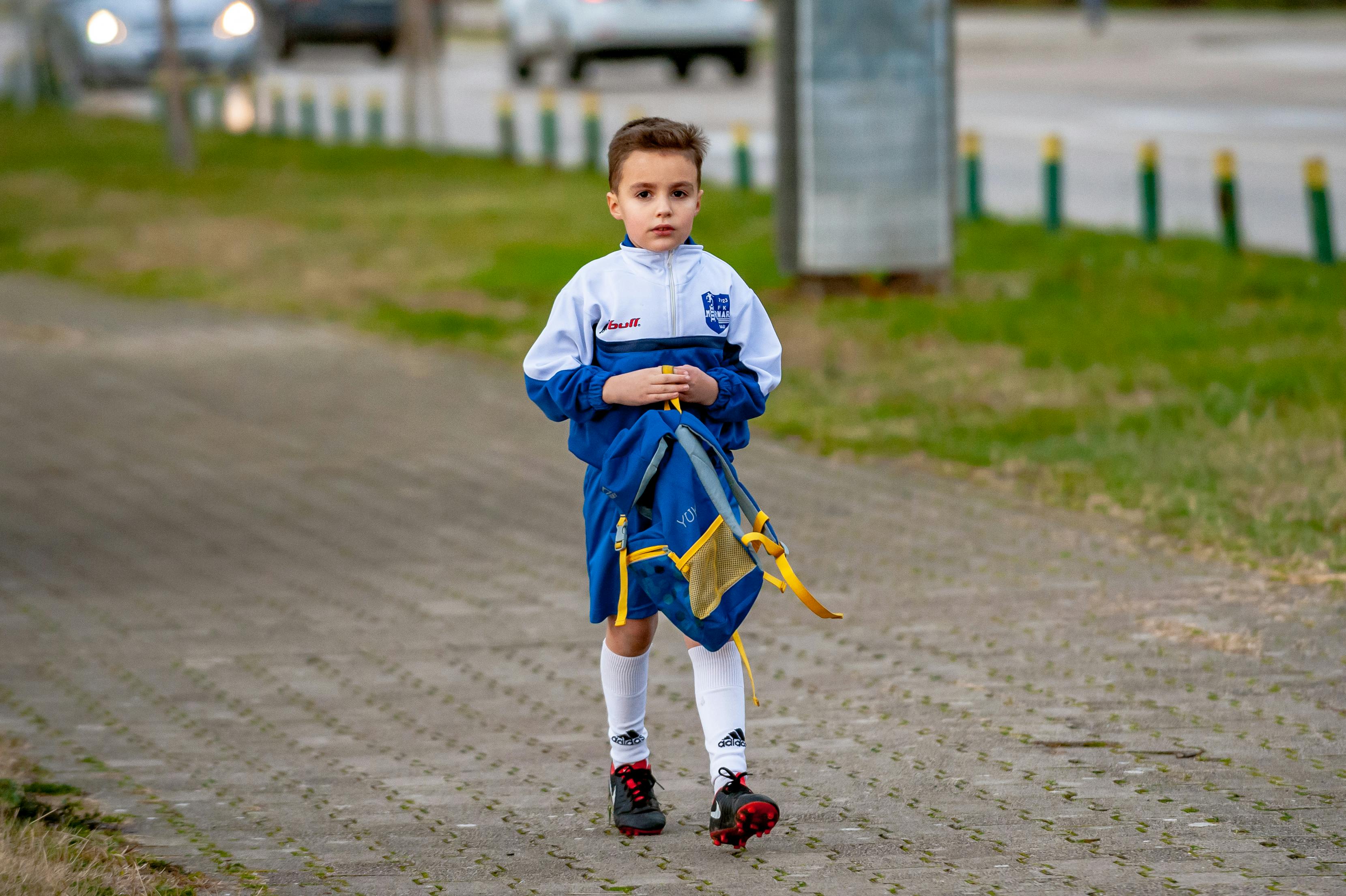 boy wearing white blue jacket walking on brick wall