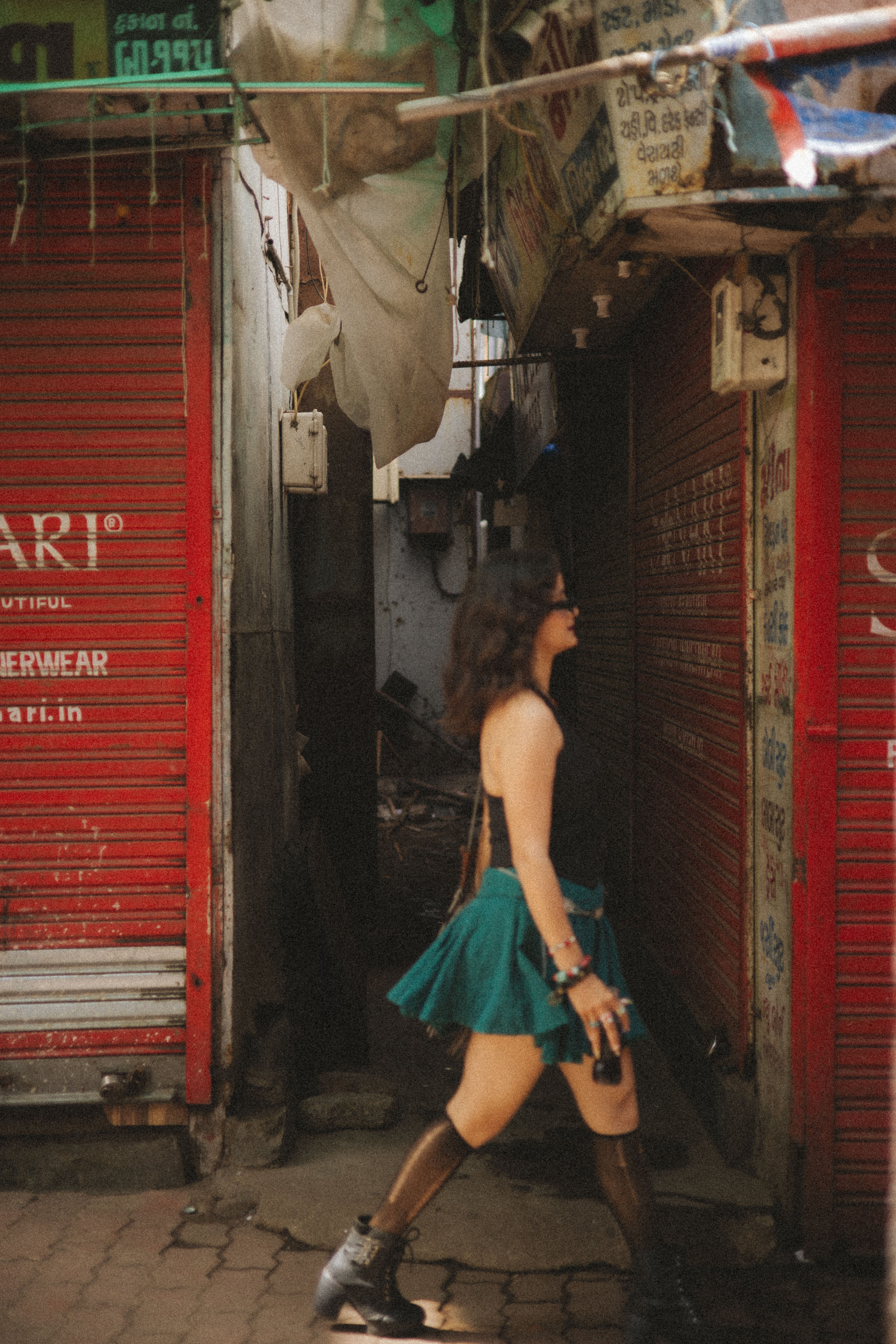 A young woman in a green skirt walks through an urban alley lined with closed shops.