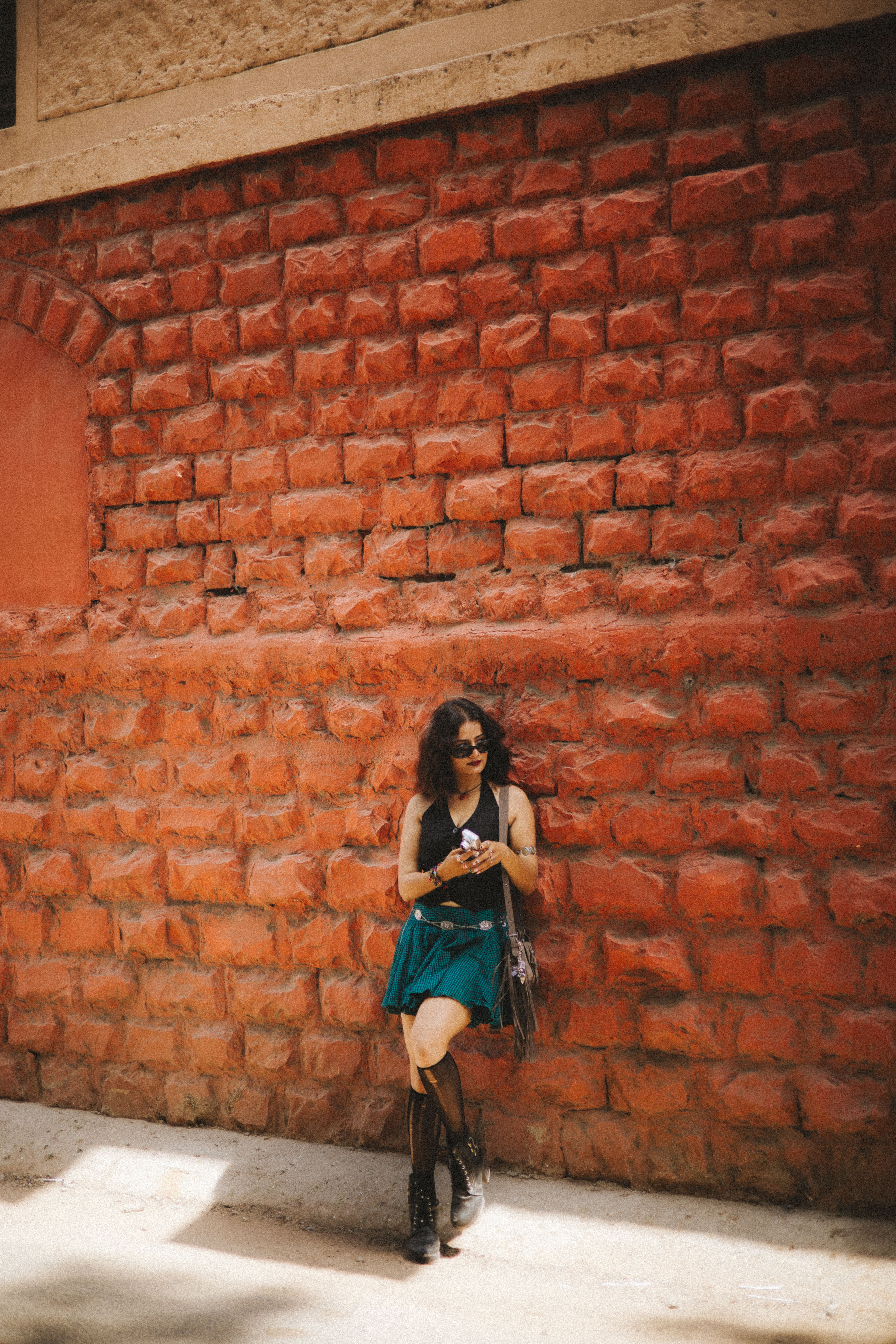 Teen woman stands against a vibrant red brick wall, capturing a stylish and edgy vibe.