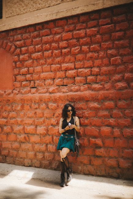 Teen woman stands against a vibrant red brick wall, capturing a stylish and edgy vibe.