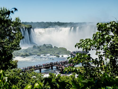 Free Tourists enjoying the magnificent view of Iguazu Falls from a wooden deck surrounded by lush greenery. Stock Photo