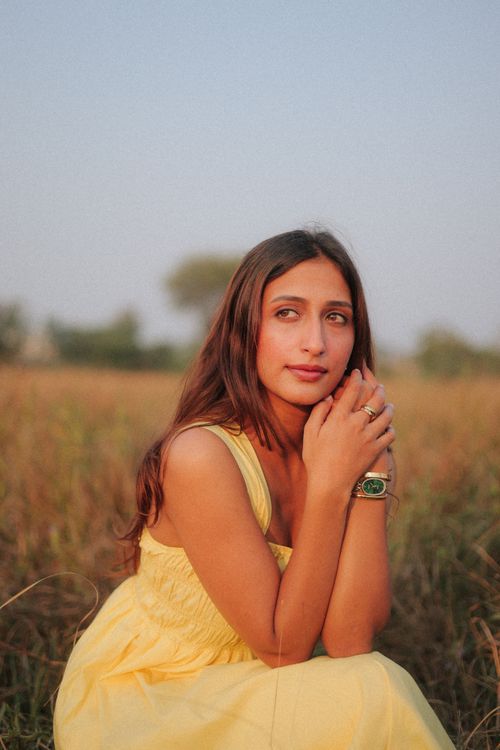 Free A young woman in a yellow dress sitting thoughtfully in a field during sunset. Stock Photo