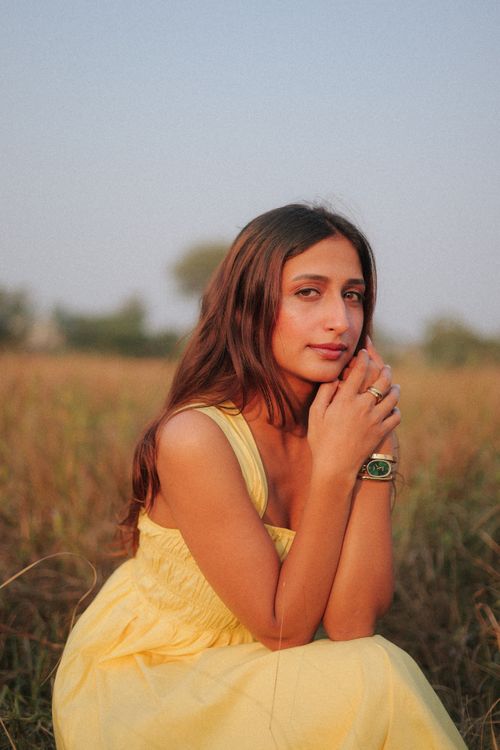 Free A young woman wearing a yellow dress sits in a scenic, grassy field under a clear sky. Stock Photo