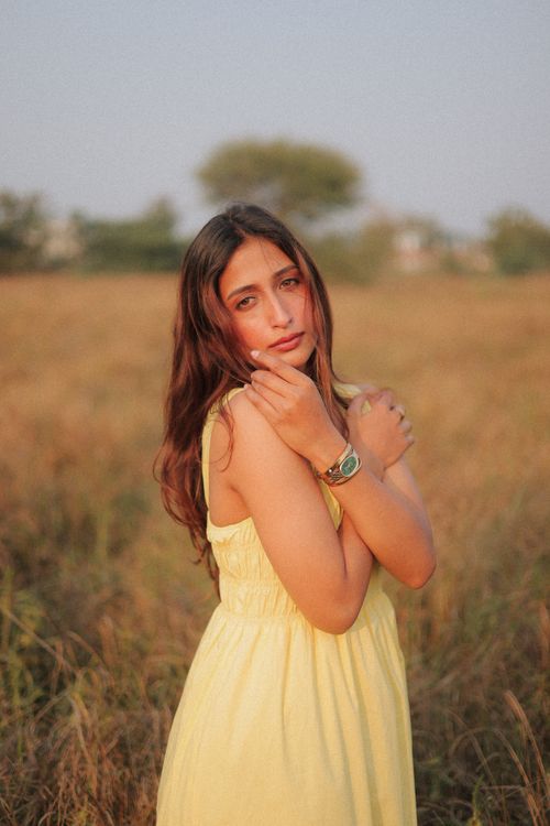 Free A young woman in a yellow dress standing in a field during daytime. Stock Photo