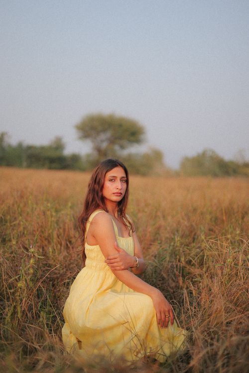 Free A woman in a yellow dress sits in a serene grassy field during sunset, evoking tranquility and natural beauty. Stock Photo