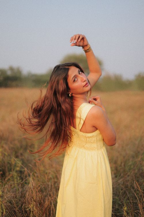 Free A young woman in a yellow dress poses gracefully in a sunny field, capturing a carefree summer vibe. Stock Photo