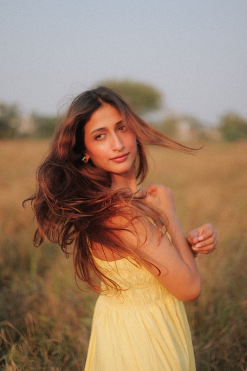 Free A woman in a yellow dress stands in a field, her hair blowing in the wind. Stock Photo