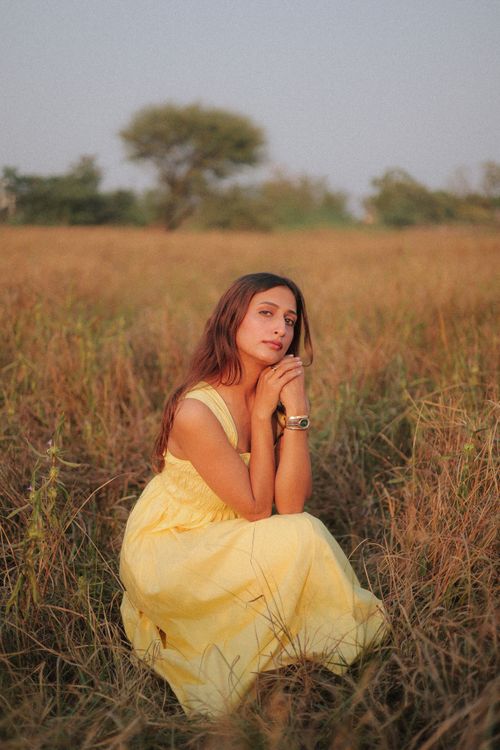 Free A woman in a yellow dress sitting in a field, reflecting a serene and peaceful mood during a warm day. Stock Photo