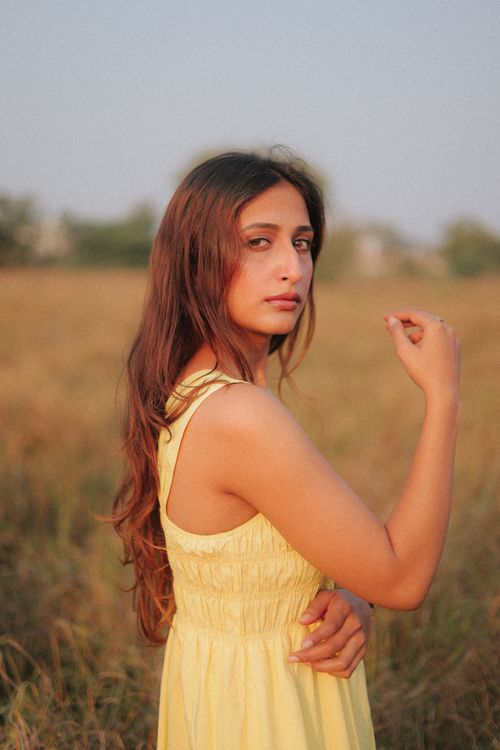 Free A young woman in a yellow dress poses in a grassy field during sunset. Stock Photo