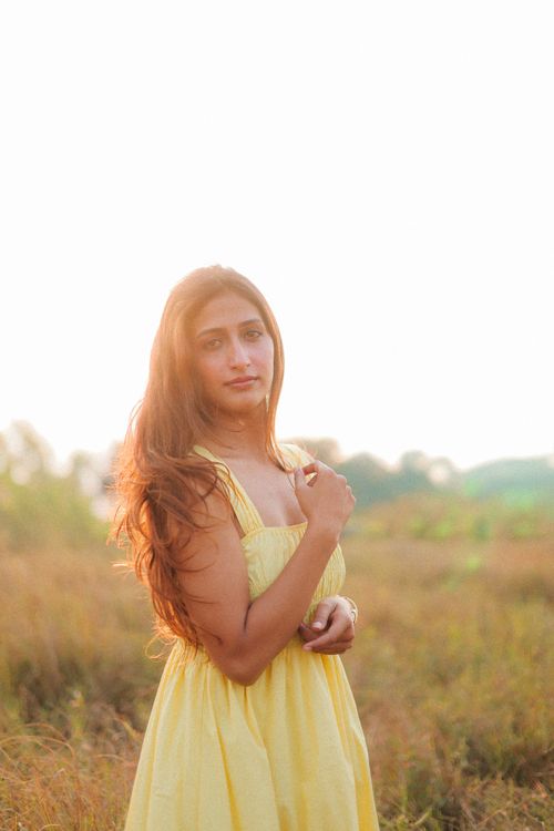 Free Portrait of a woman in a yellow summer dress standing in a sunlit field during golden hour. Stock Photo