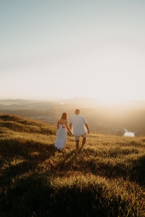 Free Romantic couple walking hand in hand on grassy hill during sunset, SP, Brazil. Stock Photo