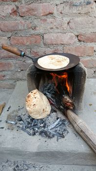Close-up of roti being cooked on a traditional tandoor with open flame, showcasing rustic Indian culinary techniques.