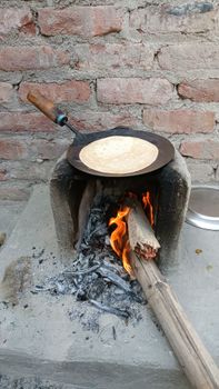 Authentic roti being cooked on a wood-fired stove outdoors, depicting traditional cooking methods.