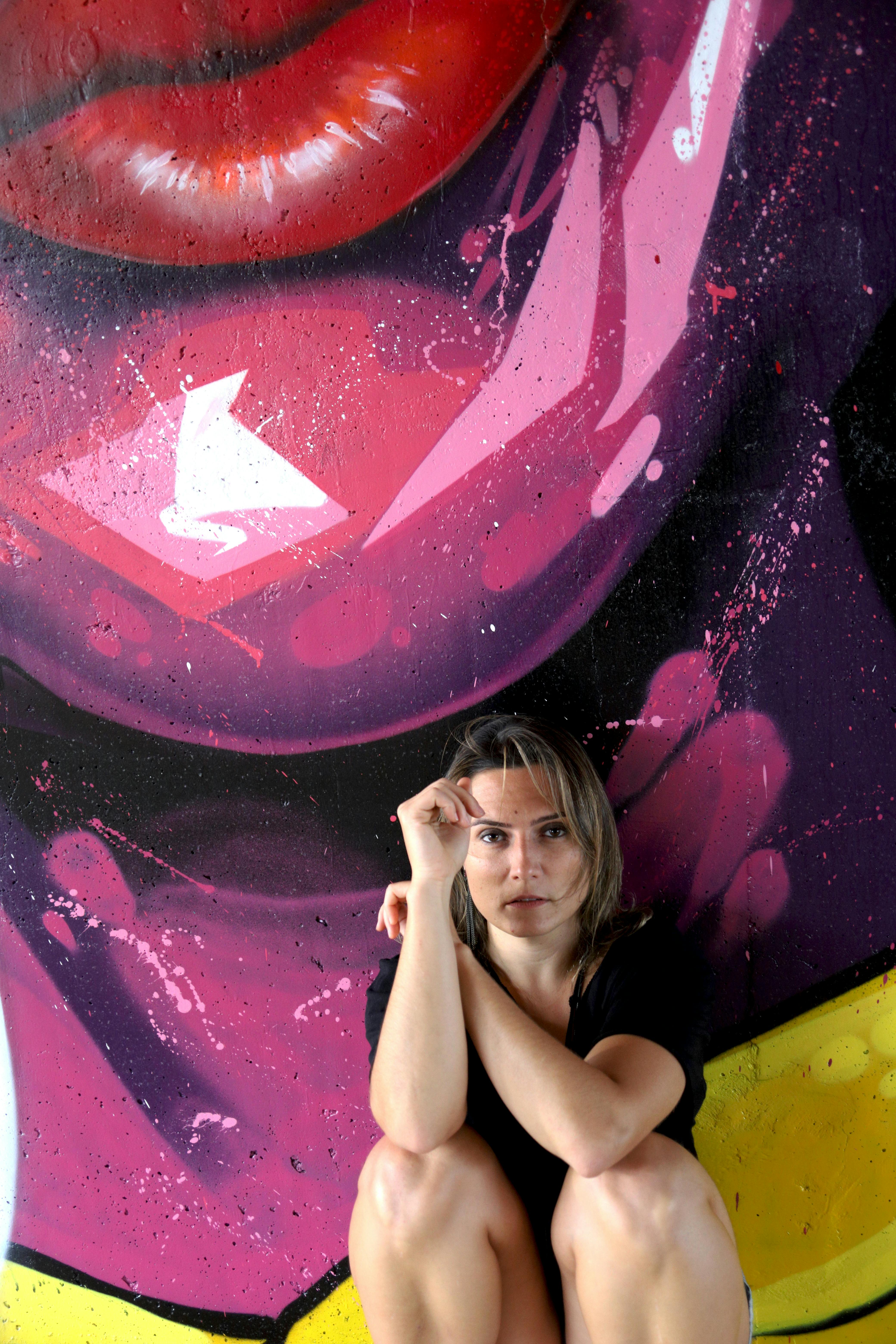 Woman sitting before a colorful graffiti mural, urban art exploration.
