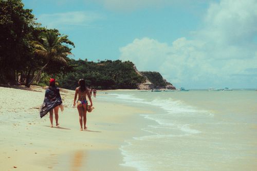 Free People enjoying a sunny day on a tropical beach with lush greenery and clear skies. Stock Photo