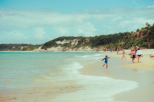 Free Families enjoying a sunny day at a scenic tropical beach with lush green cliffs. Stock Photo