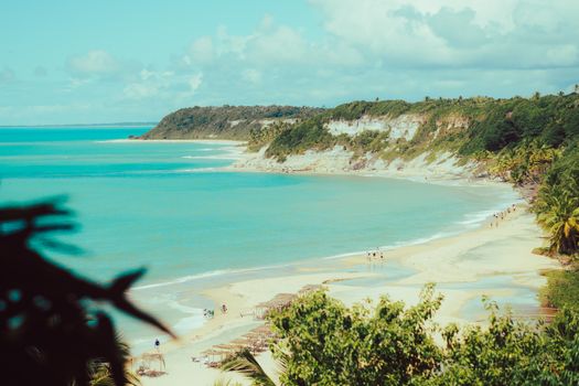 Breathtaking view of a tropical beach with turquoise waters and lush cliffs under a bright sky.