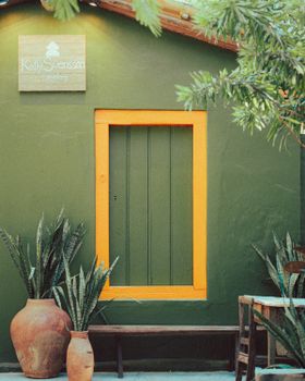Charming green house with vibrant orange window frame, surrounded by potted plants, exuding a cozy ambiance.