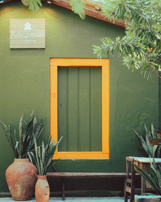 Charming green house with vibrant orange window frame, surrounded by potted plants, exuding a cozy ambiance.