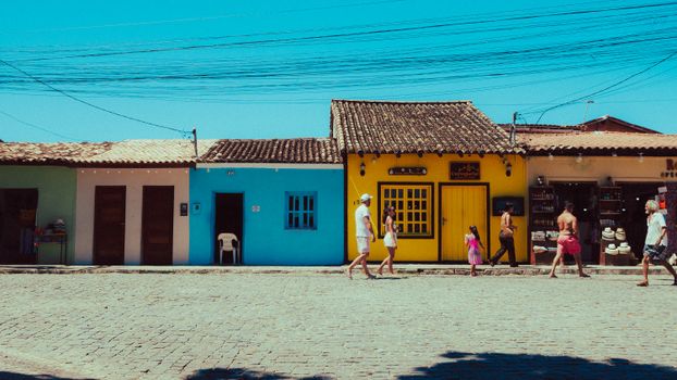People walking by colorful traditional buildings on a sunny day.