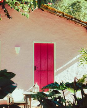 A serene outdoor scene featuring a pink house with a vibrant pink door, enhanced by foliage and natural light.