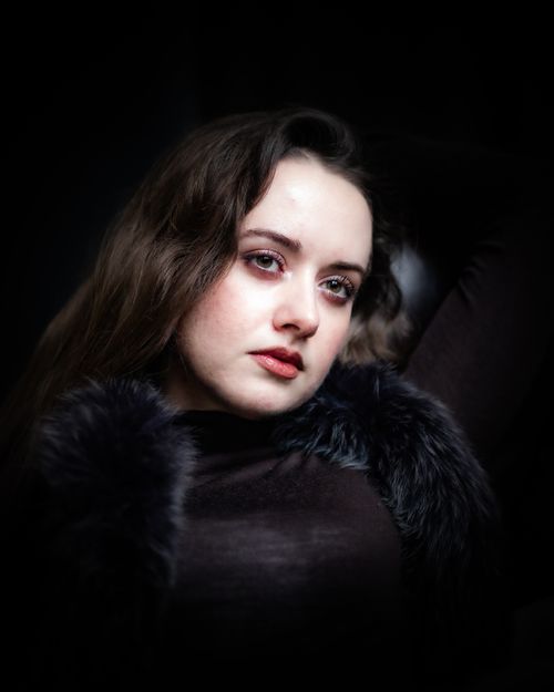 Free Moody portrait of a woman with long hair and fur collar, set against a dark backdrop. Stock Photo