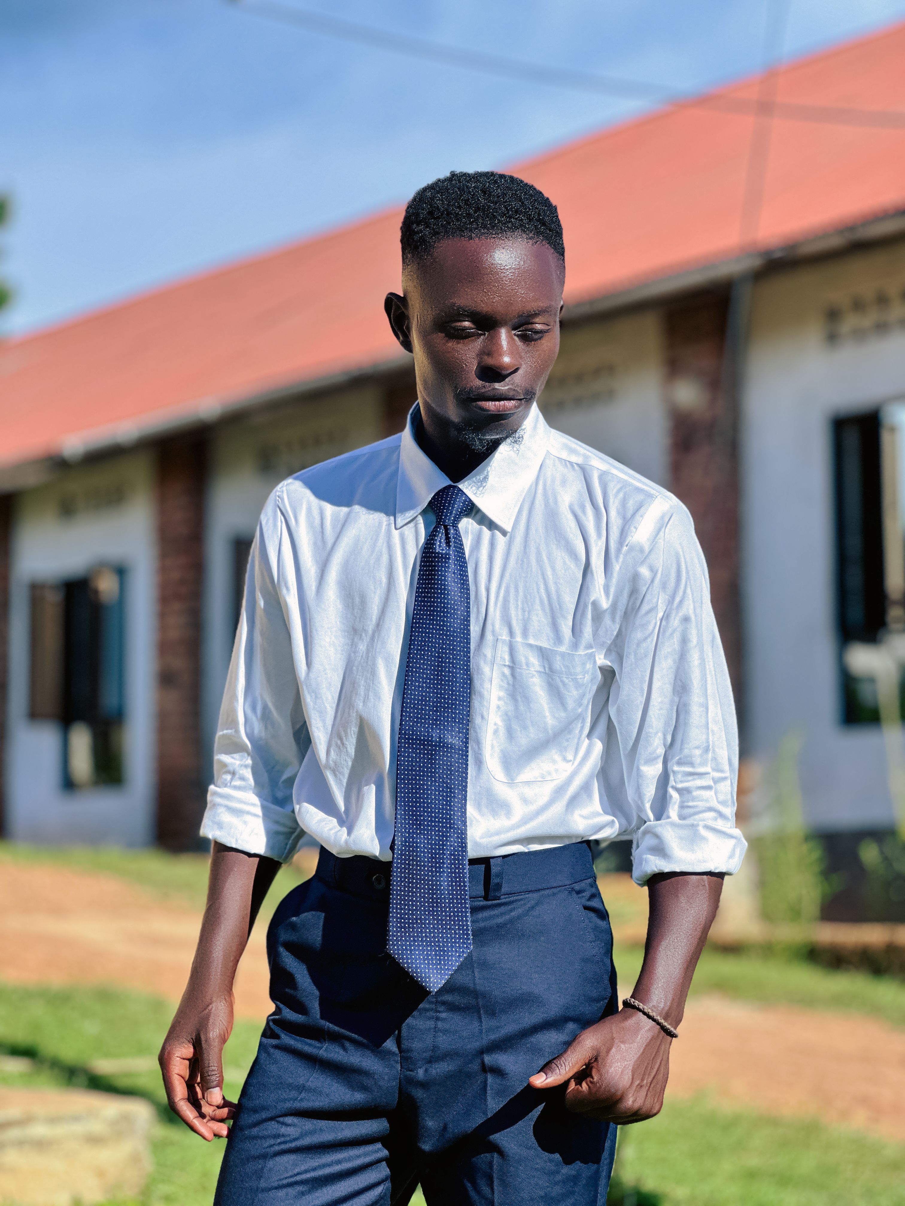 Young man in formal attire standing outside a brick building on a sunny day.