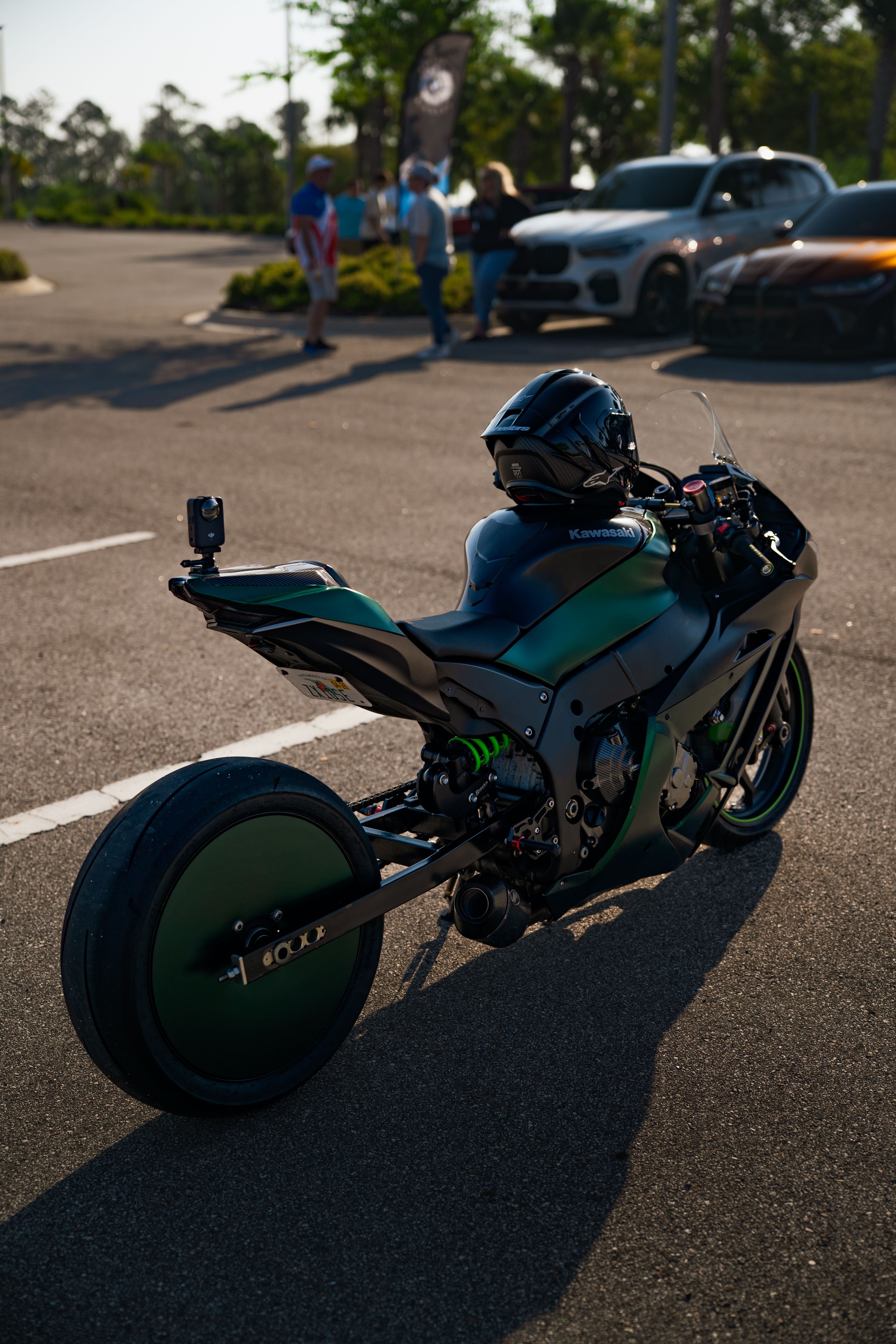 A modern sport motorcycle parked in a sunlit lot with cars and people in the background.