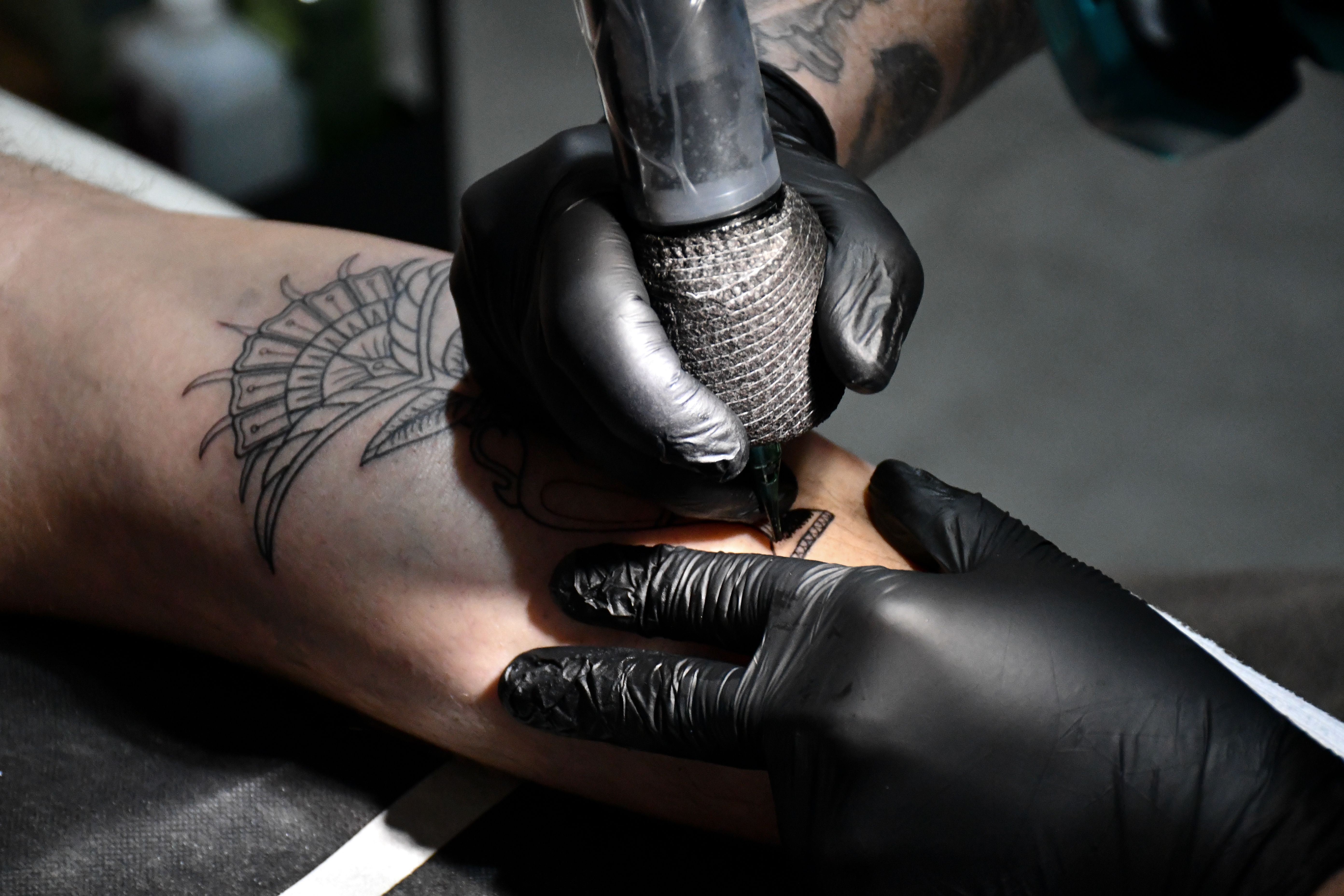 Tattoo artist creating an intricate fine line design on a forearm