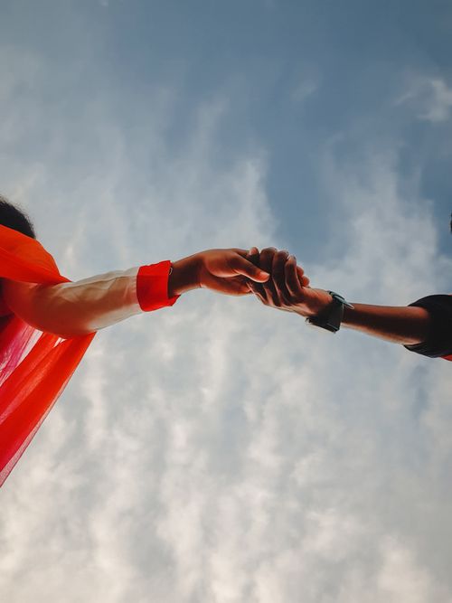 Free Low angle view of two people holding hands with a blue sky, symbolizing connection and support. Stock Photo