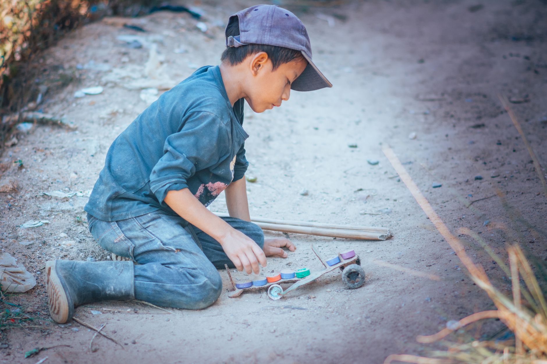 A young boy intently playing with a homemade toy car on a dirt path.