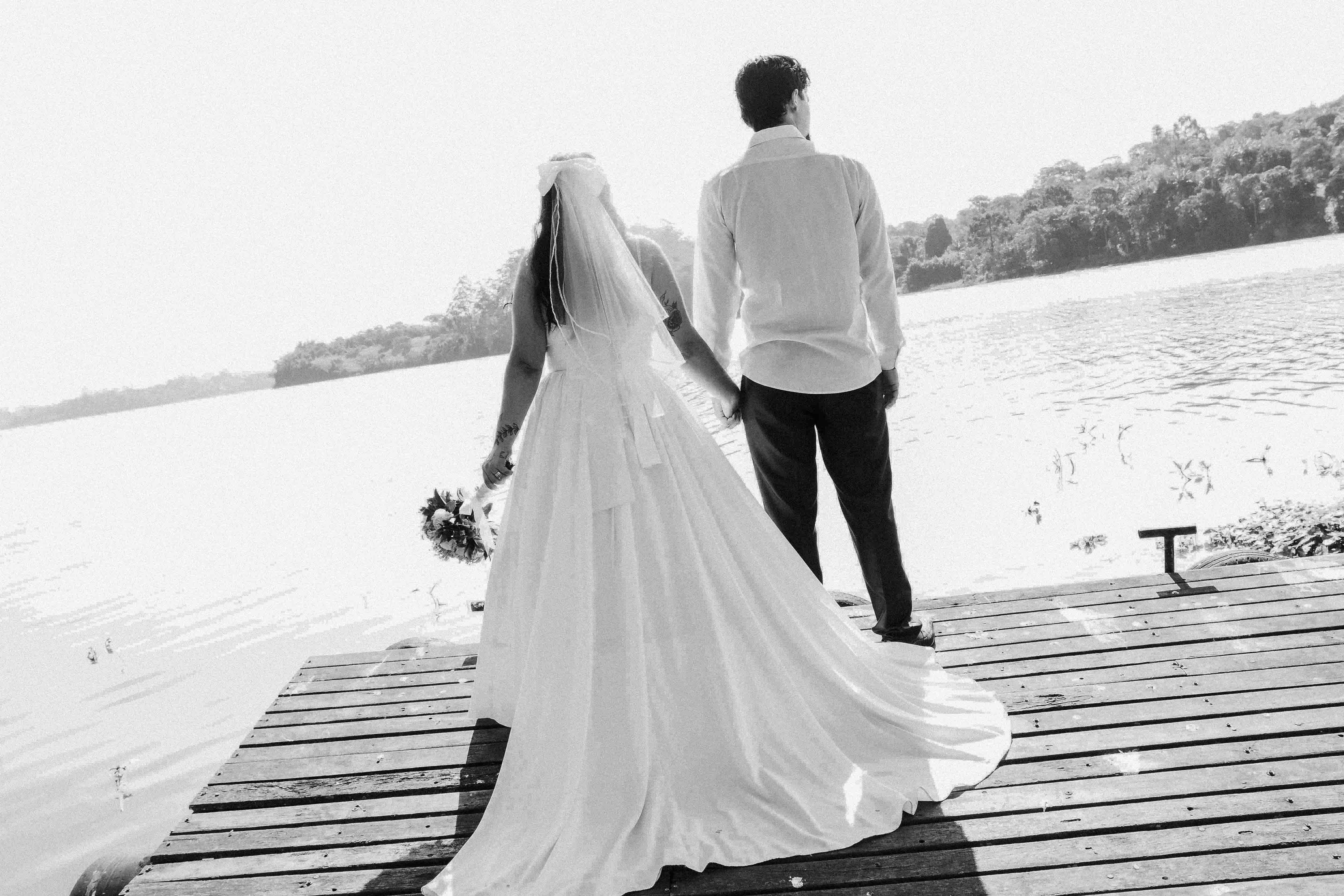 A romantic black and white image of a couple in wedding attire standing by a serene lake.