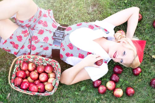Kobieta W Szaro Białych Różowych Kombinezonach Z Nadrukiem Na Trawie Obok Czerwonych Jabłek
