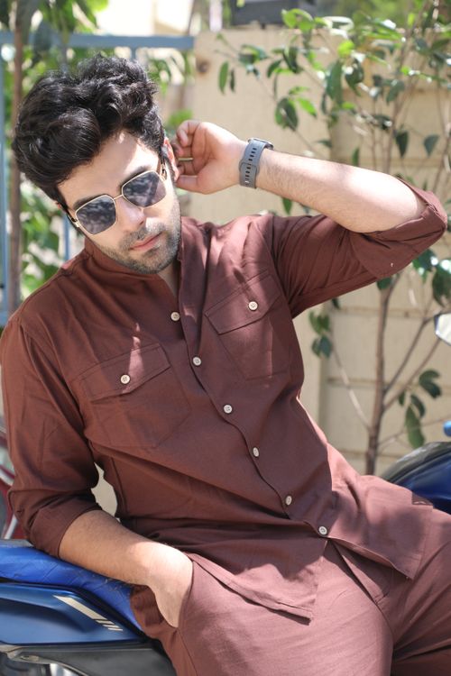 Free Stylish man in sunglasses and brown outfit sitting outside on a sunny day. Stock Photo