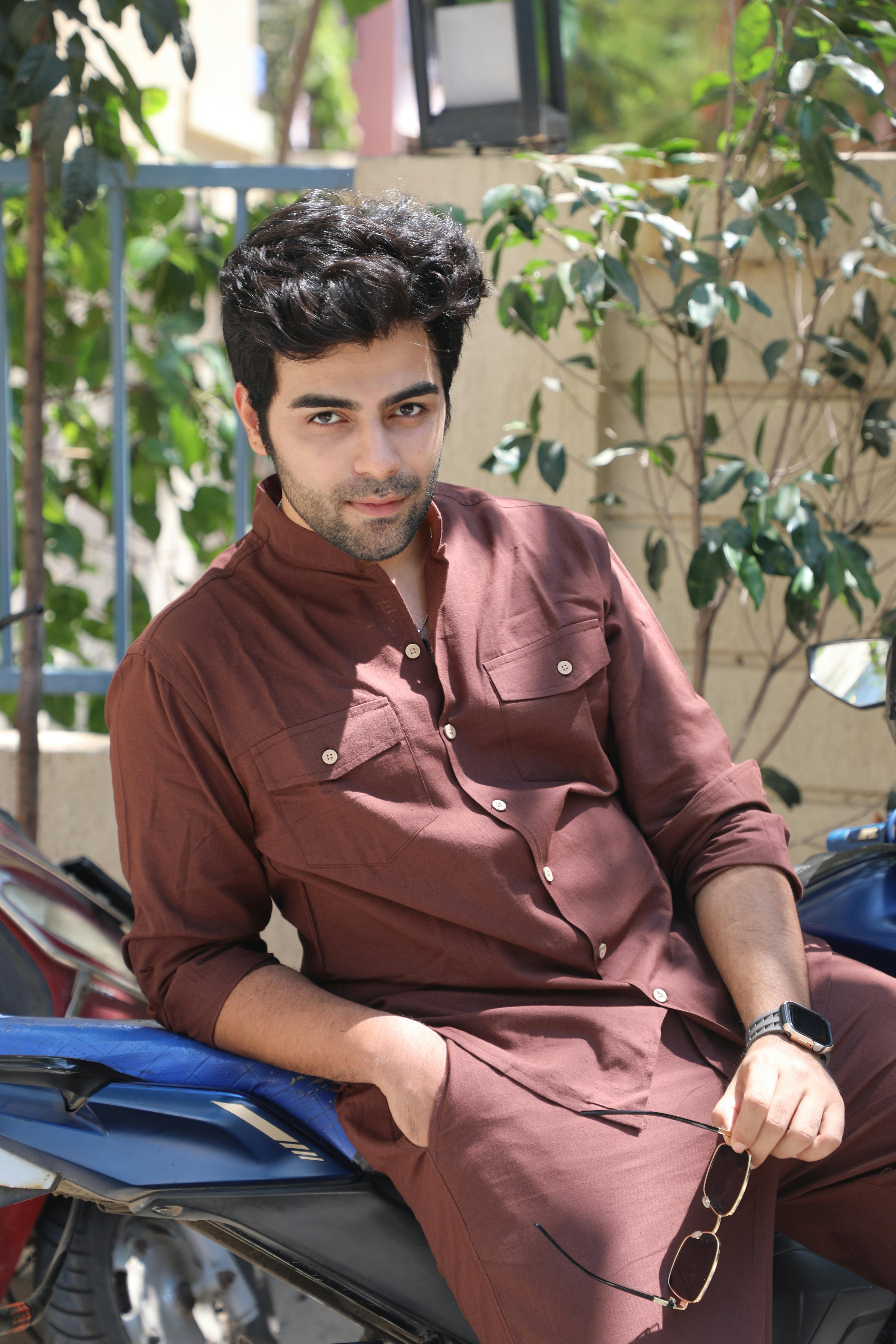 Young man sitting on a motorcycle outdoors, wearing a brown outfit, exuding confidence.