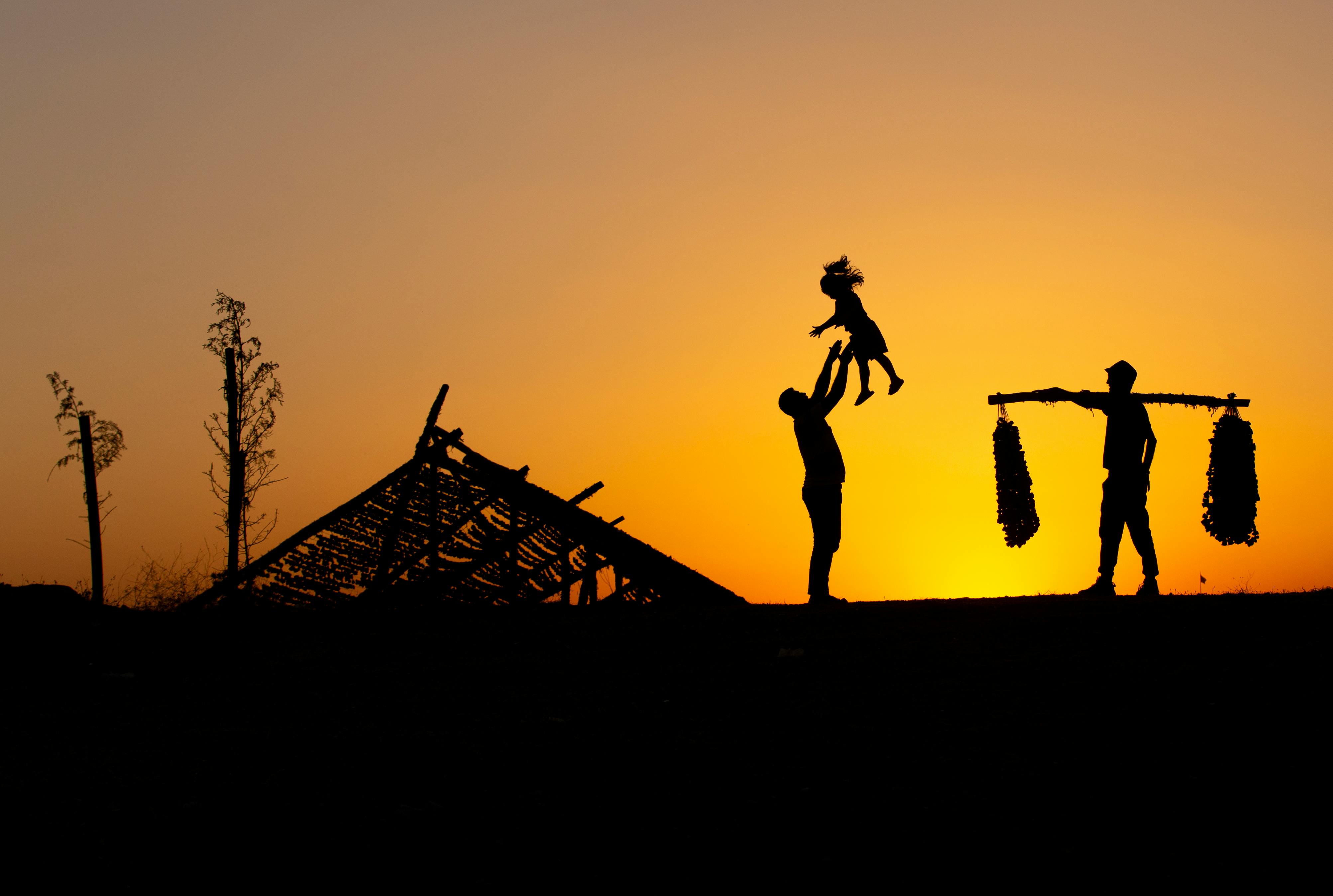 Silhouette of a family enjoying a sunset, with vibrant orange sky backdrop.