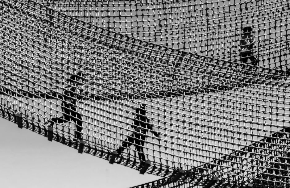 Silhouettes of children playing on a suspended rope bridge, captured in black and white.