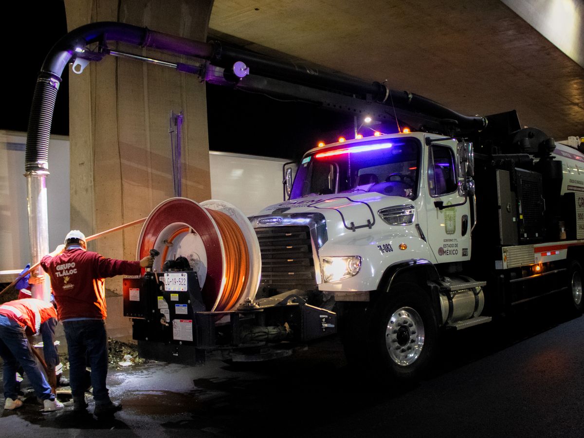 Men working with industrial drain cleaning machinery at night on urban streets