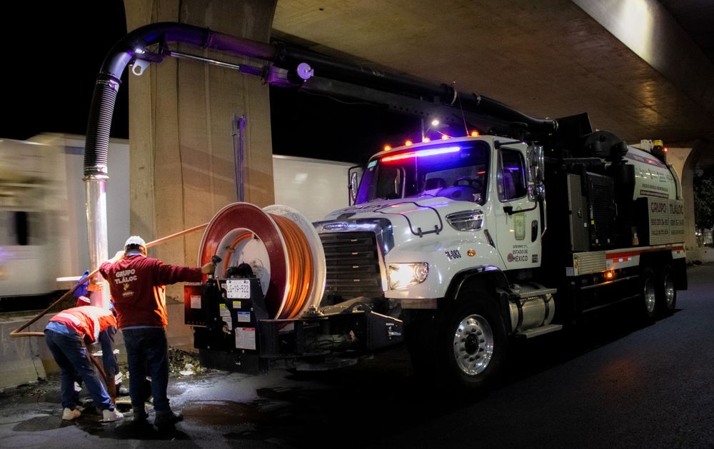 Jetter truck with its high-pressure hose reel deployed, crew working the line